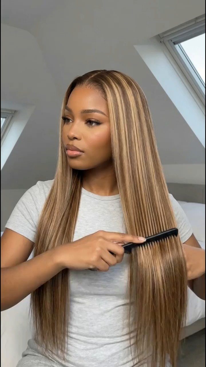 Woman combing long blonde hair with lighter highlights in a bright room