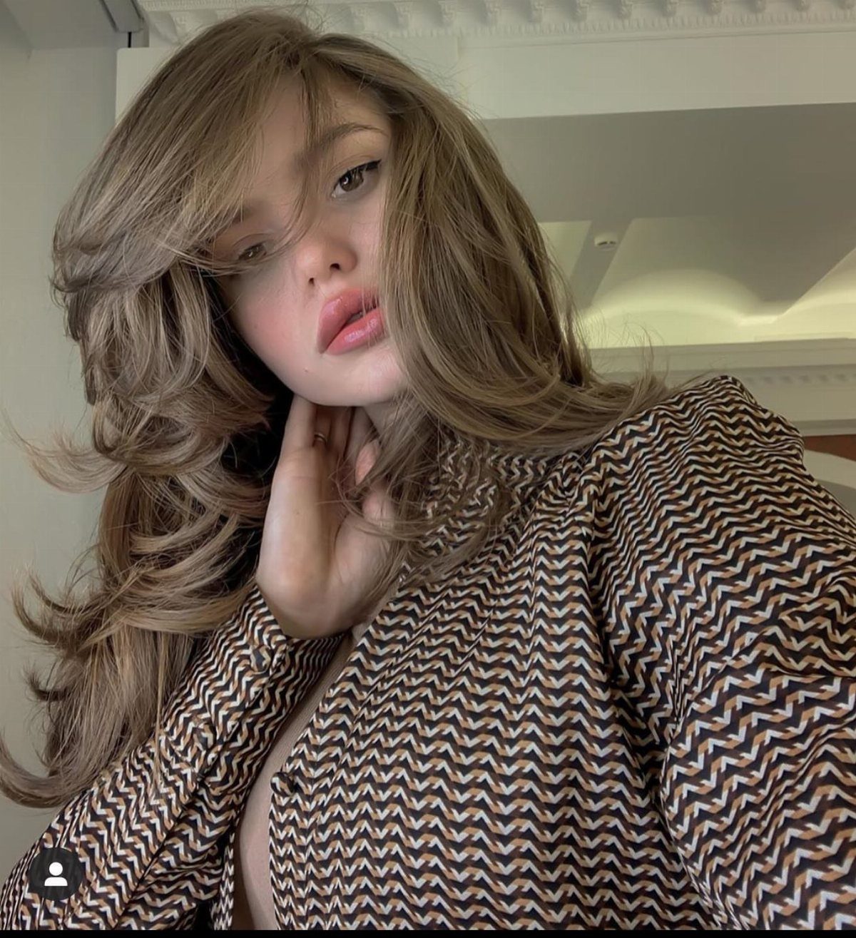 Woman with long layered beige-blonde hair and darker roots posing indoors