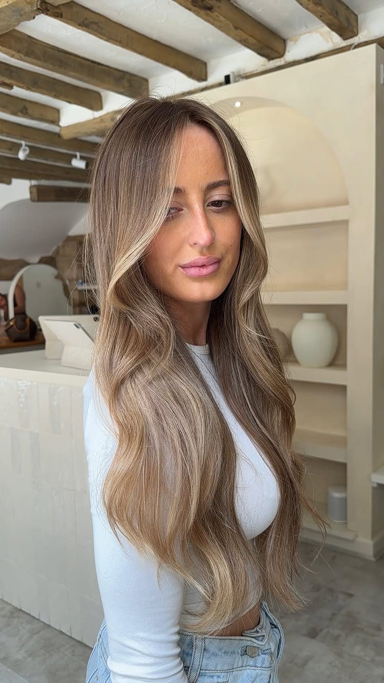 Woman with long, warm brownish blonde waves and darker roots