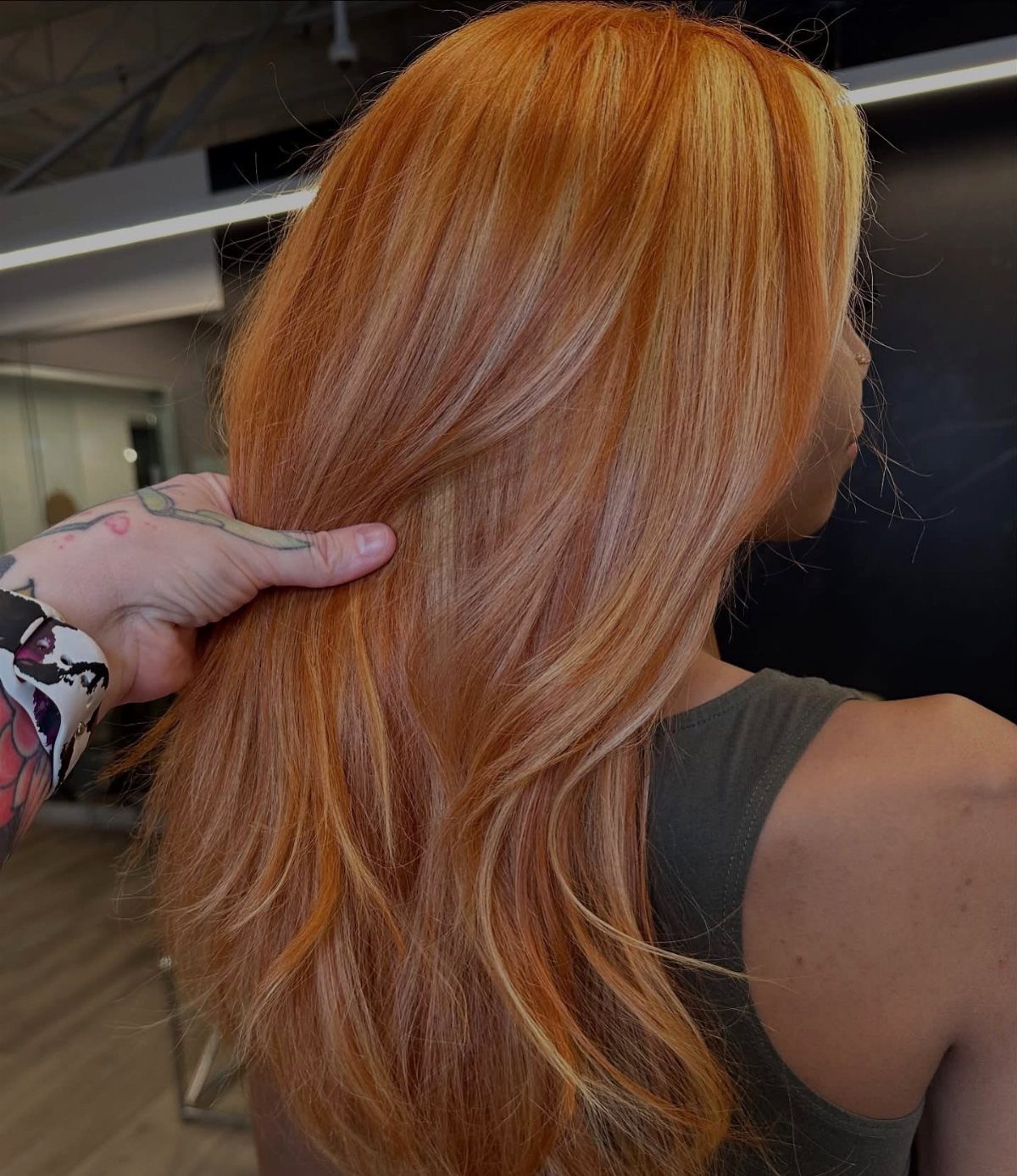 Long copper blonde hair shows warm orange and golden tones in a salon