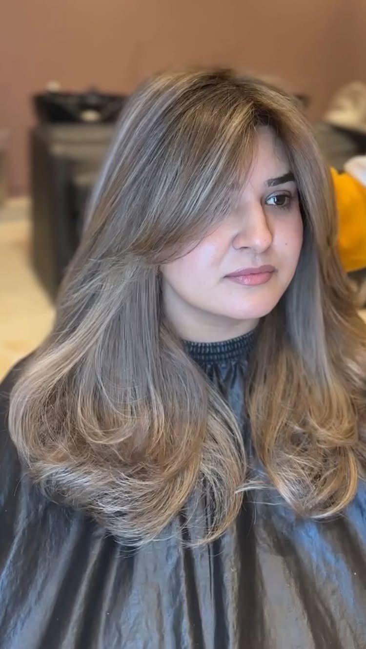 Woman with long, layered dark blonde hair and lighter highlights in a salon