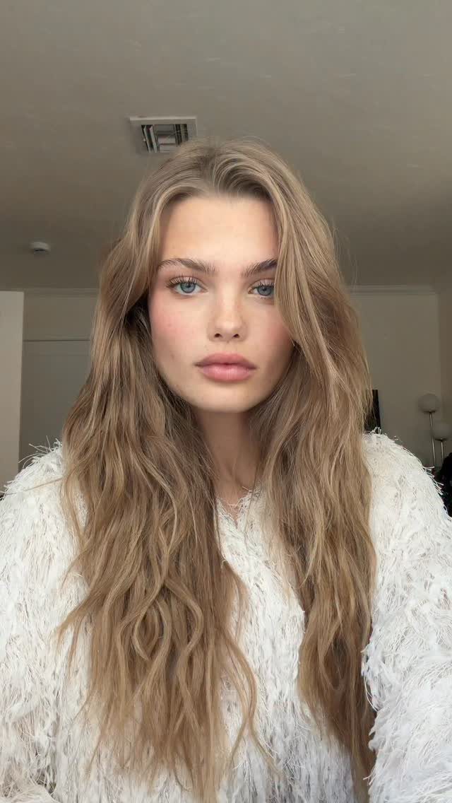 Woman with long, wavy dark natural blonde hair and a center part