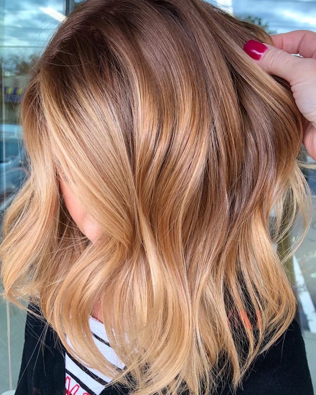 Blonde hair with dark roots and lighter highlights, parted by a hand