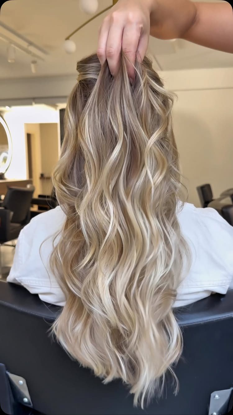 Long sandy blonde waves with beige tones lifted by a hand in a salon