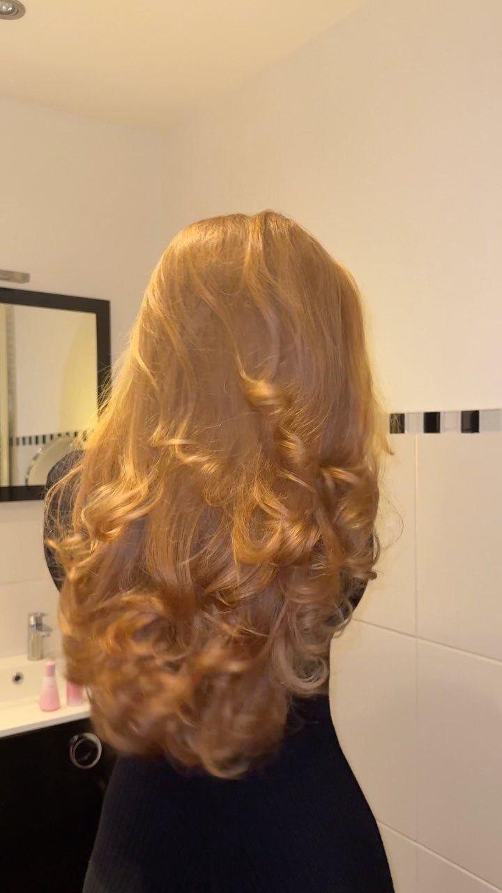 Long golden copper-blonde curls cascade down a person's back in a bathroom