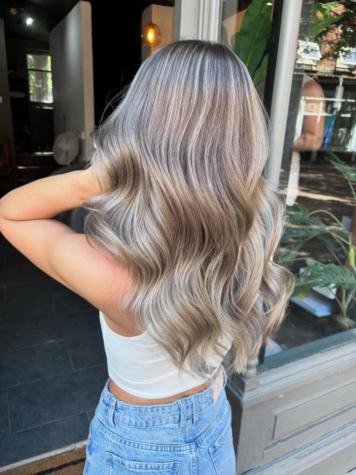 Long wavy blonde hair with cool ash-gray highlights seen from behind