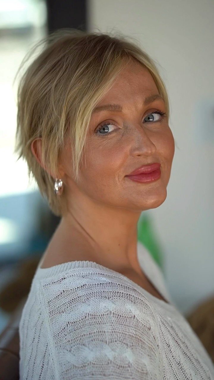 Woman with a tousled dark blonde pixie bob and long side-swept bangs
