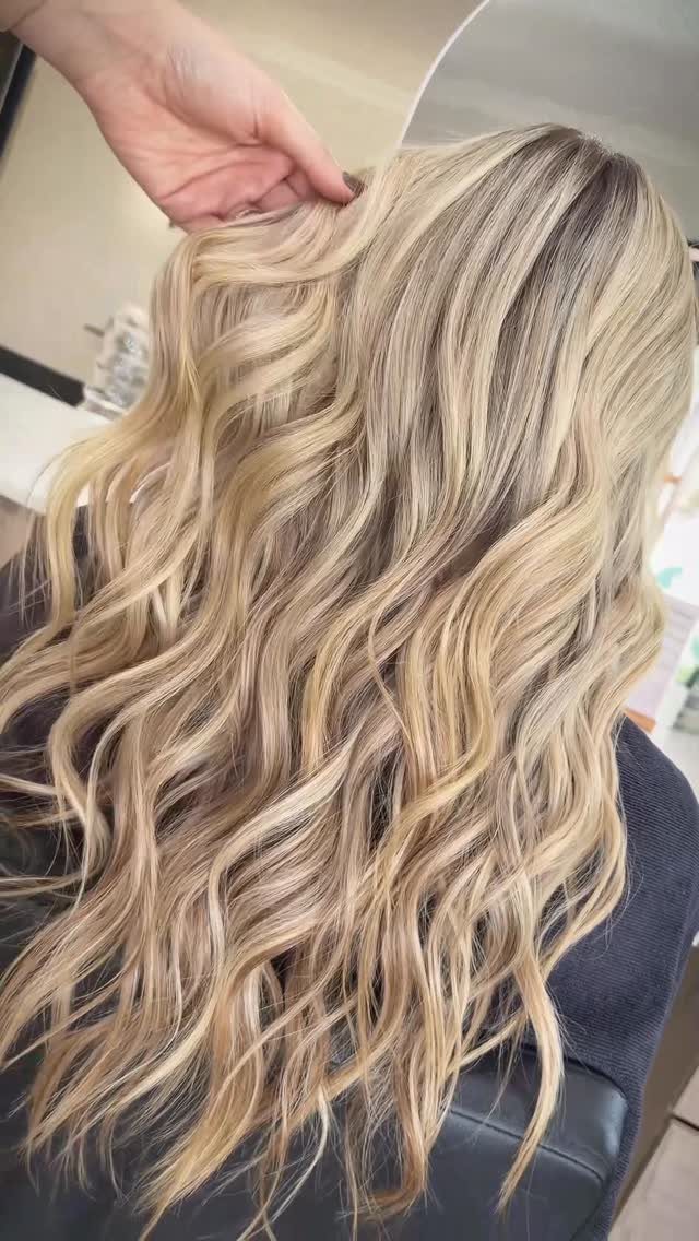 Long blonde waves show darker roots and blended beige and ash tones