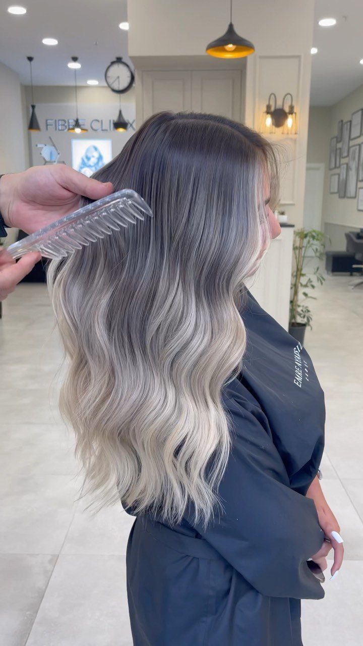 Long wavy hair fades from dark roots into light blonde ends in a salon.