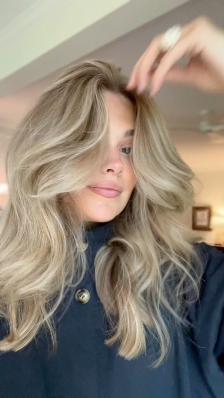 Woman lifting her blonde waves to show darker roots and blended color
