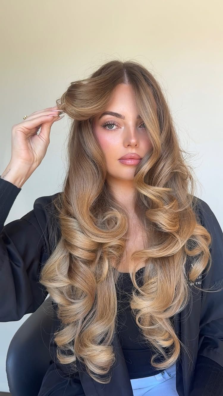 Woman posing with long blonde waves, darker roots, and curled layers