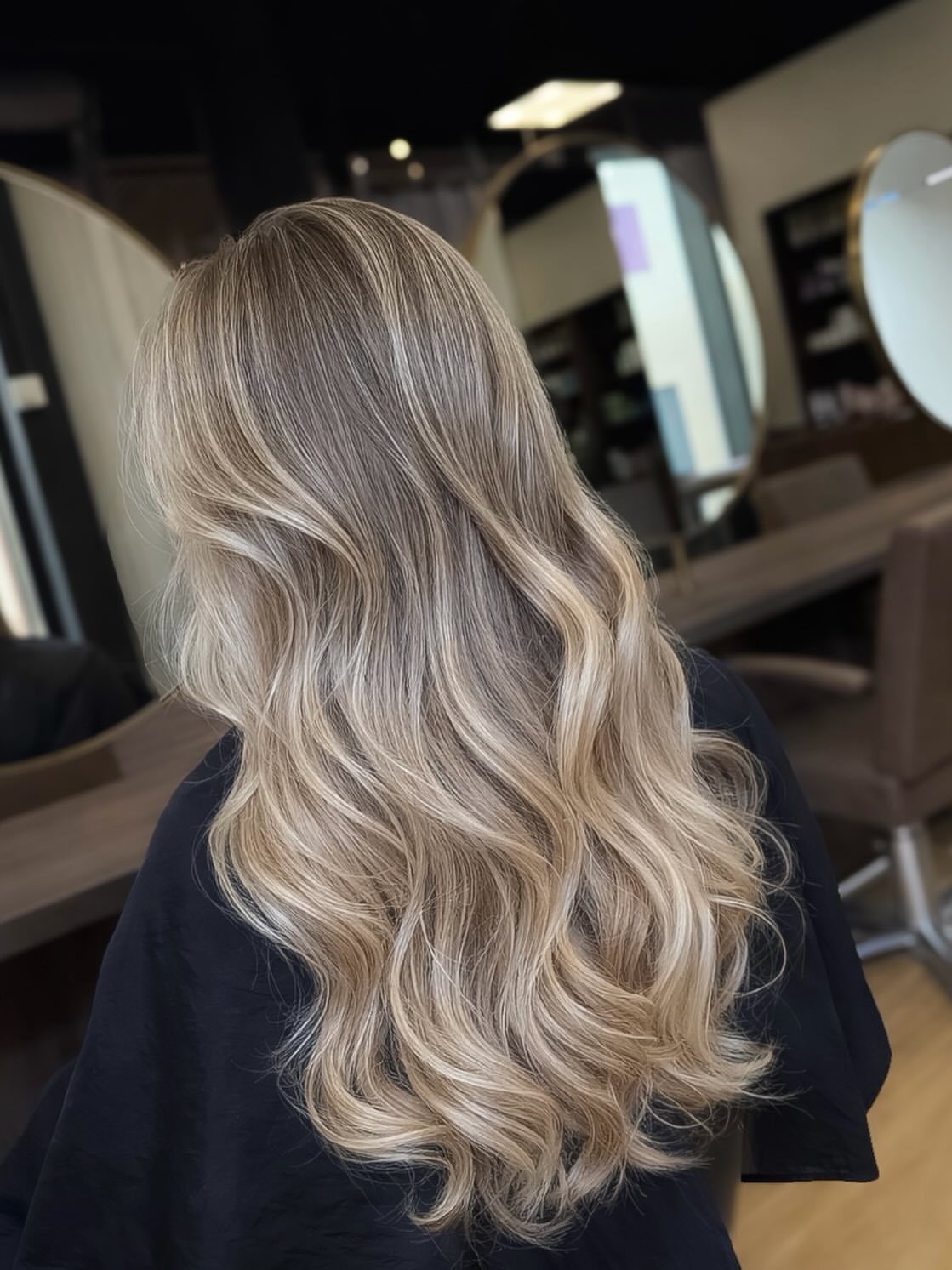 Long blonde balayage hair shines in loose, dimensional waves in a salon
