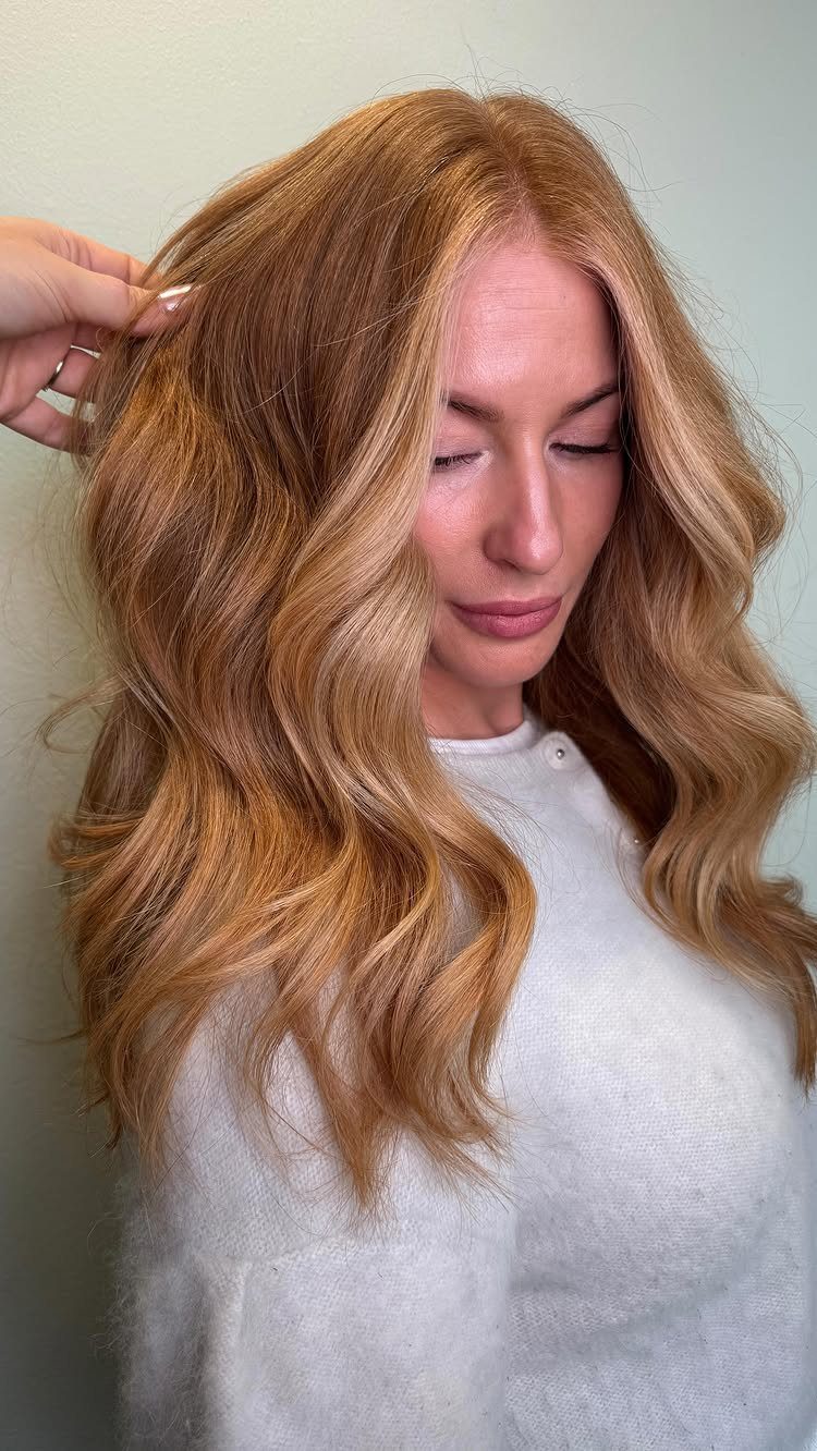 Long wavy apricot blonde hair with darker roots, lifted by a hand
