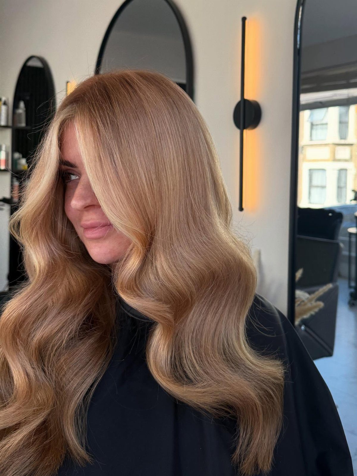 Woman showing long brown hair with warm strawberry-blonde highlights in a salon