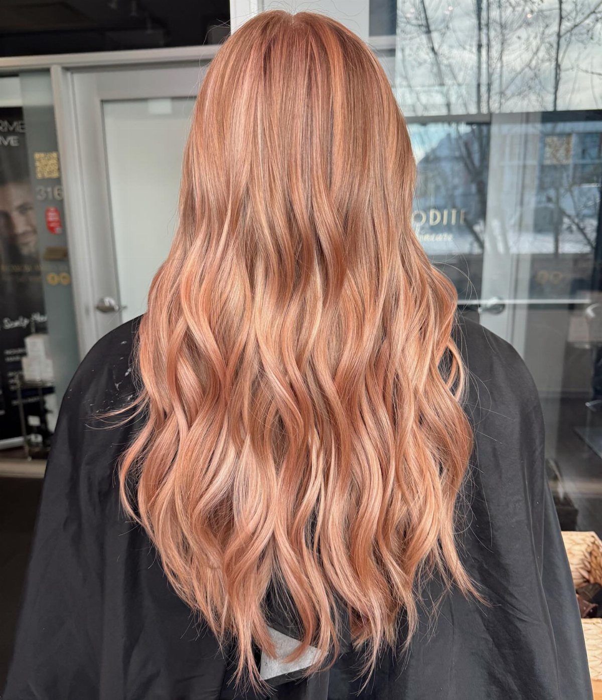 Long rosy golden strawberry blonde waves shown from behind in a salon