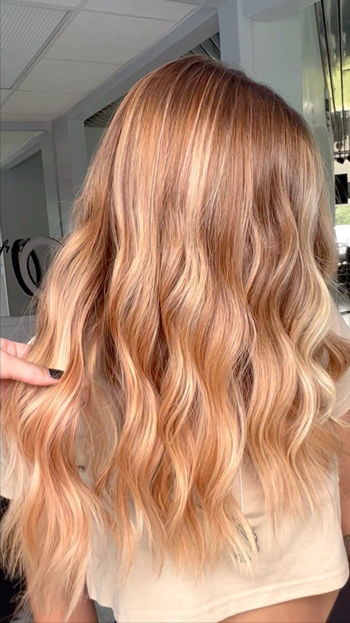 Wavy strawberry blonde hair fades from darker roots to peachy blonde ends