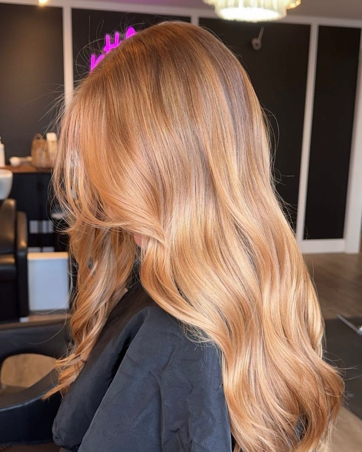 Warm blonde waves with darker roots flowing down a seated salon client's back