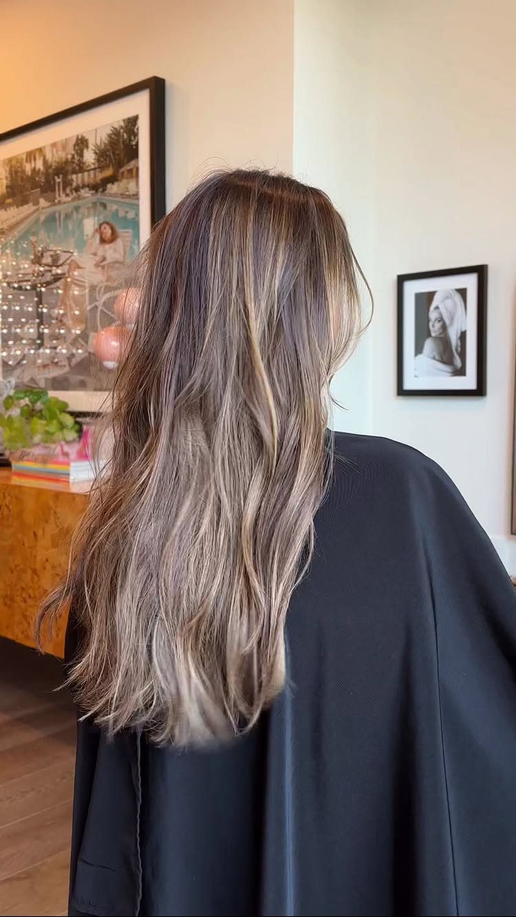 Long wavy brown hair with subtle golden highlights over a black salon cape