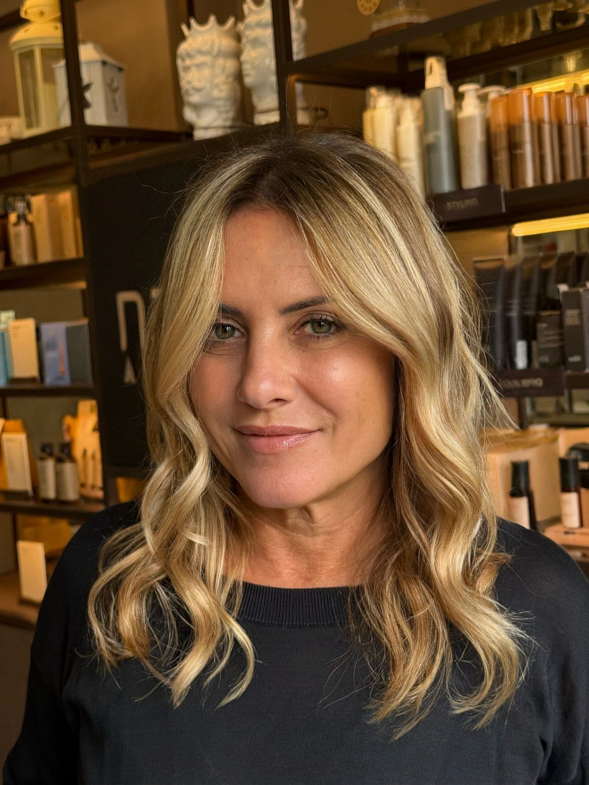 Woman with wavy champagne blonde hair and darker roots in a salon