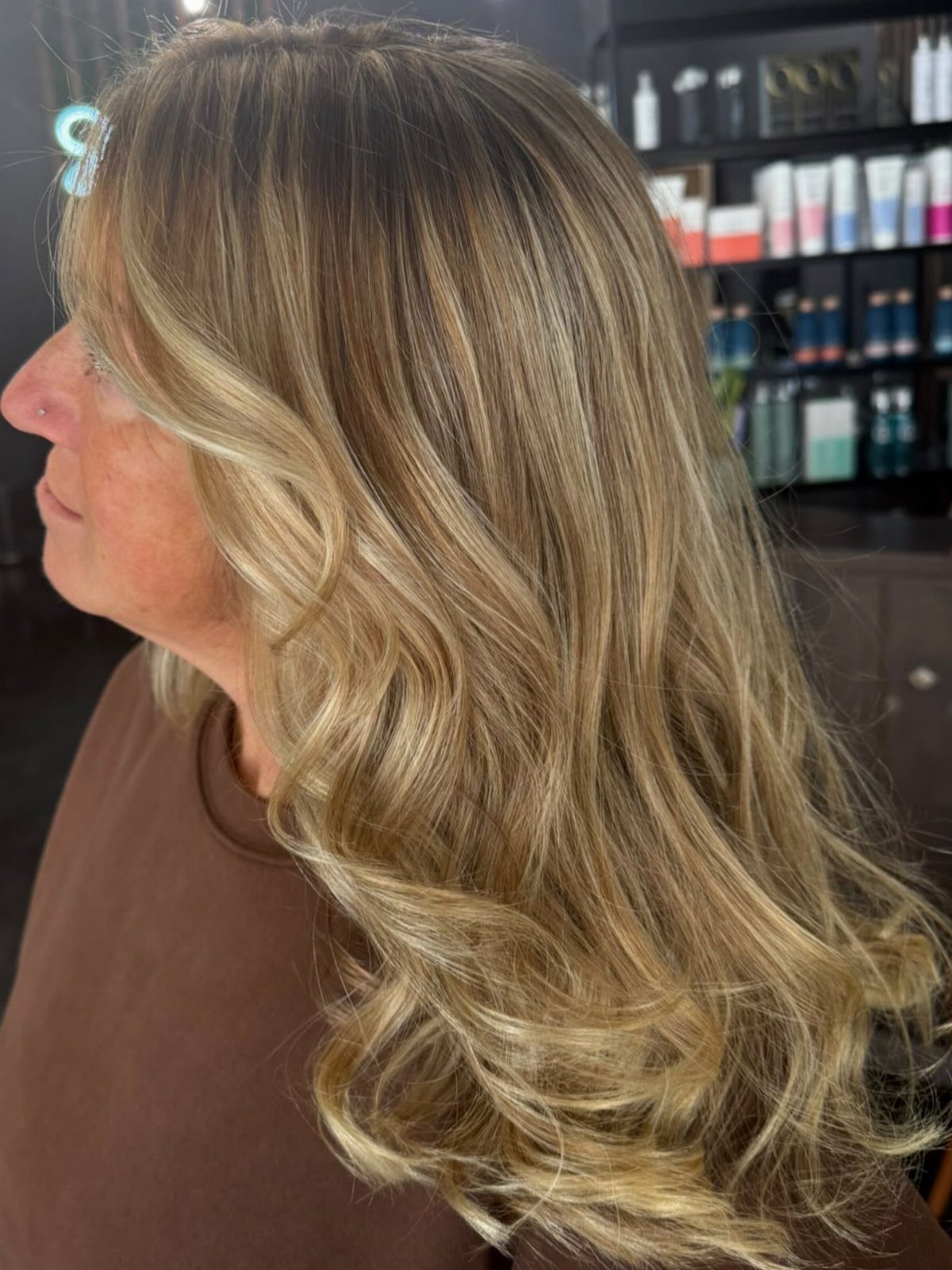 Long wavy golden blonde hair with darker roots in a salon
