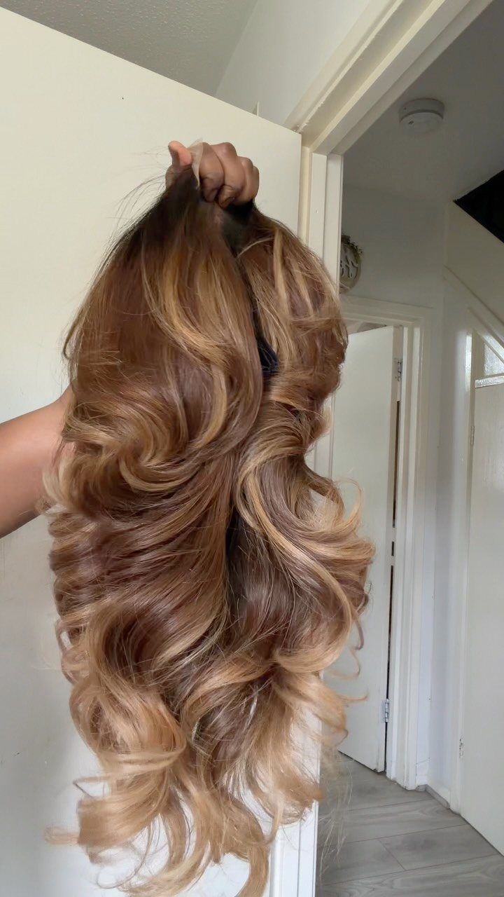 Curled dark honey blonde hair transitions into lighter honey-blonde lengths