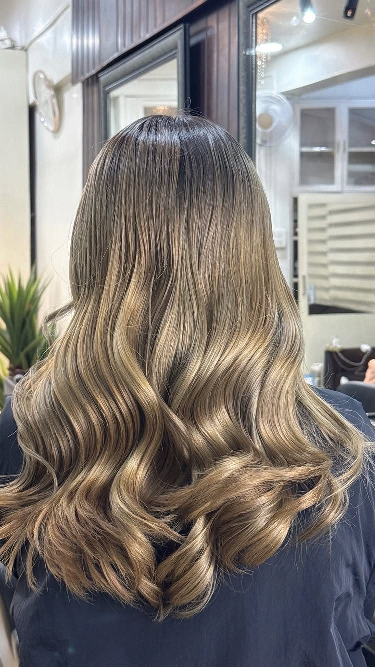 Long wavy honey ash blonde hair with dark roots in a salon