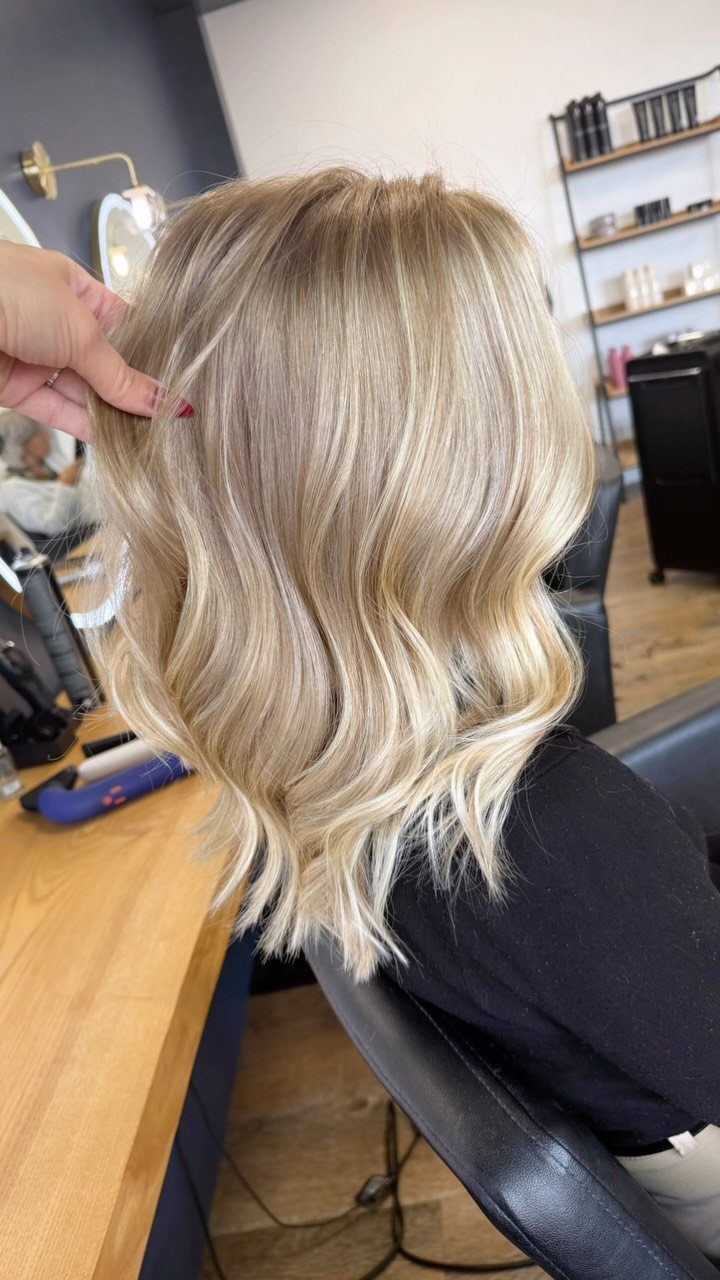 Wavy honey blonde balayage with darker roots in a salon chair