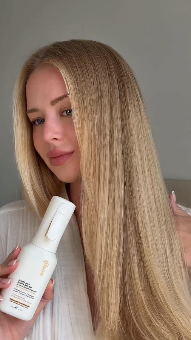 Woman with long, straight light honey blonde hair holding a white hair product bottle