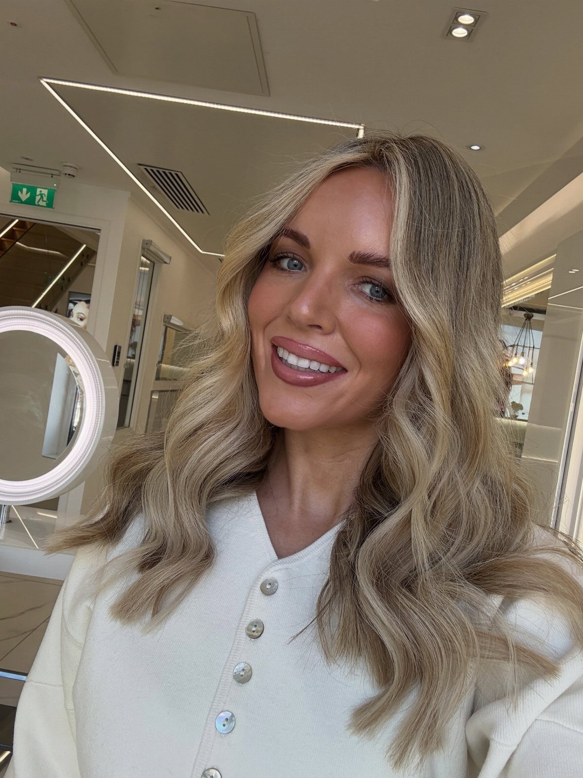 Woman displaying long, wavy light brown hair with warm honey blonde highlights in a salon