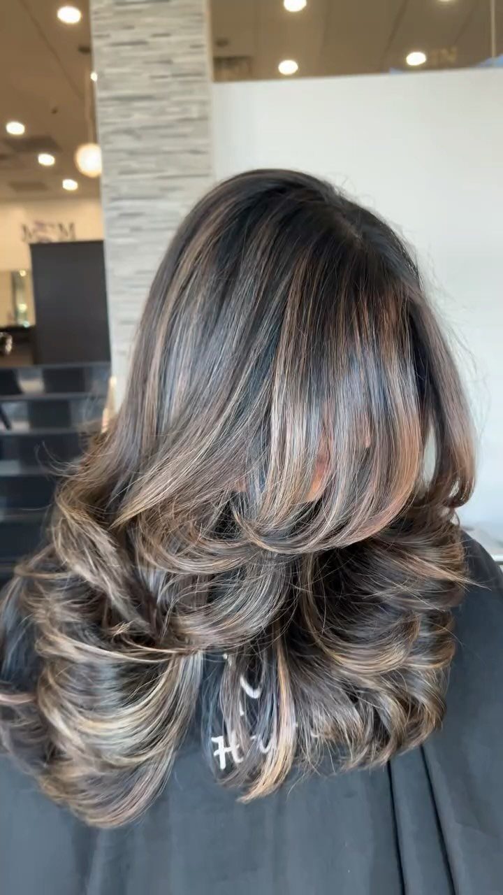 Layered dark hair with honey-beige balayage highlights curling at the ends