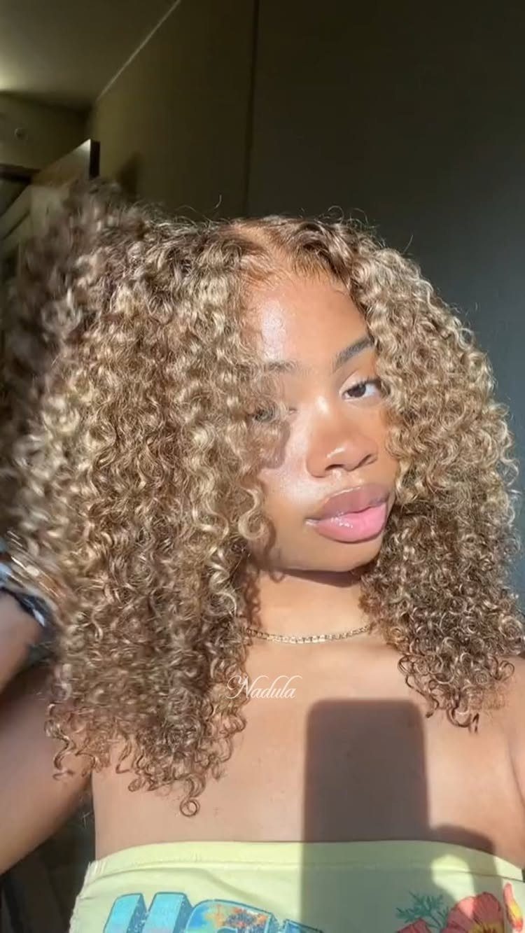 Long honey-blonde curls with darker roots frame a person's face