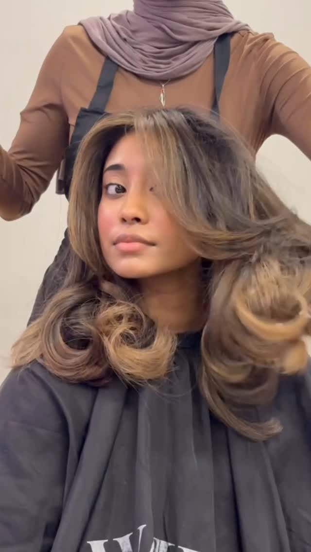 Young woman with long curls and honey-brown face-framing hair in a salon