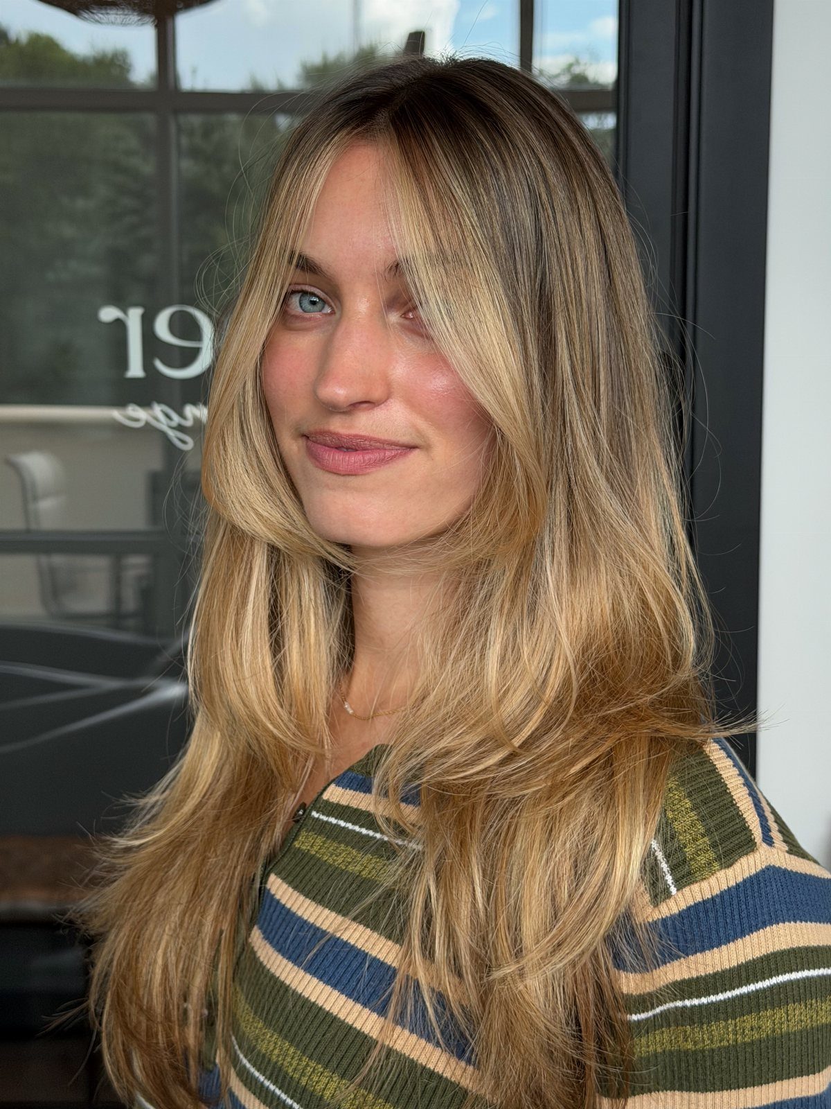 Woman showing long honey bronde hair with darker toasted roots and loose waves