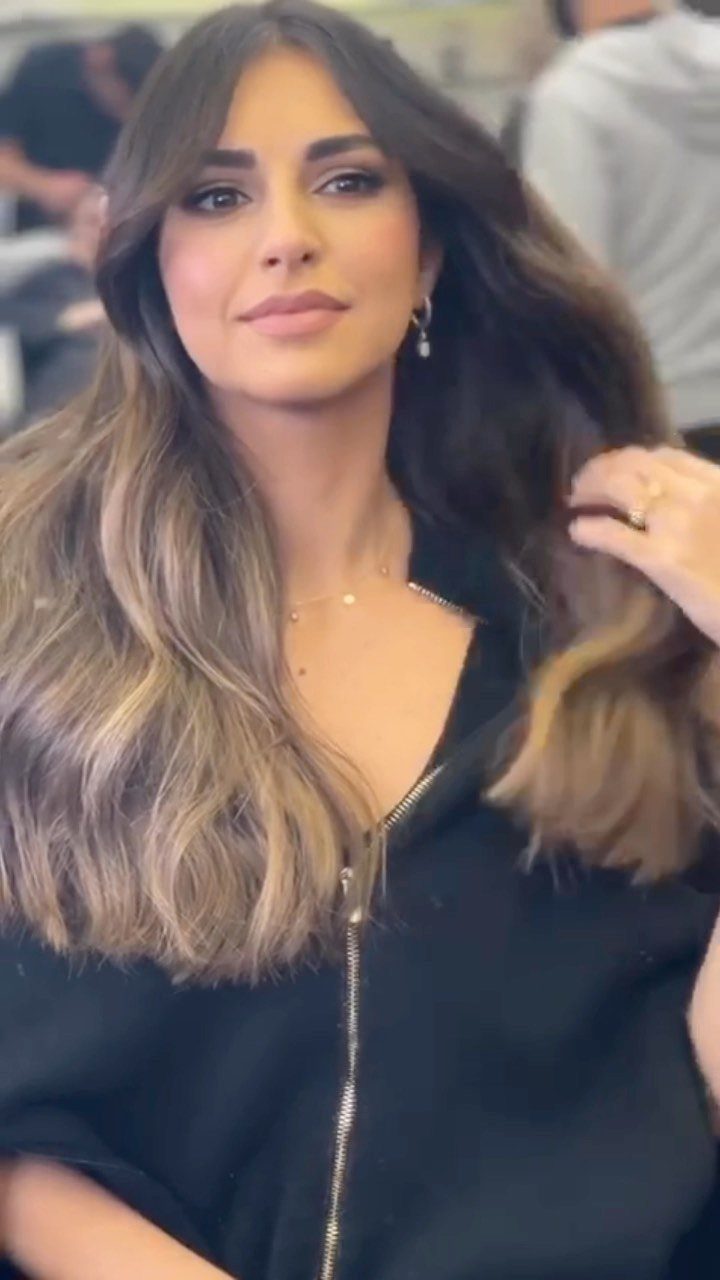 Woman with long dark brown waves and bronze-honey balayage highlights