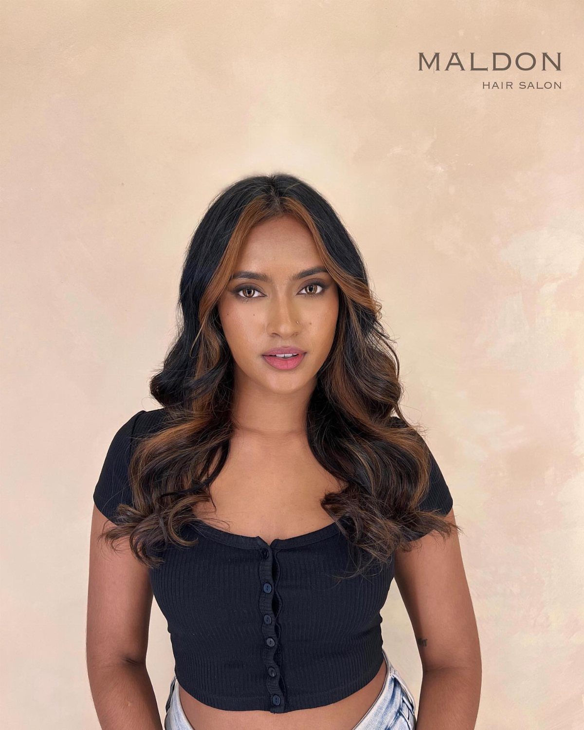 Woman with dark wavy hair and honey-brown face-framing highlights