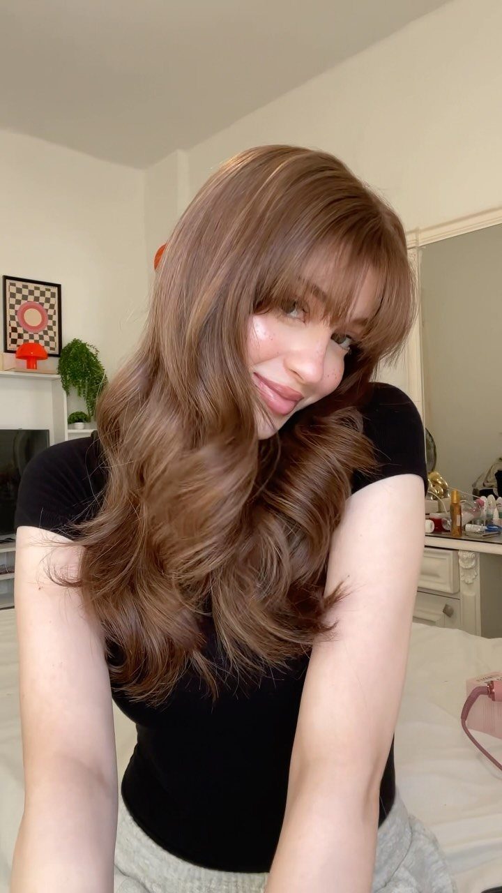 Long honey brunette hair with soft layers, warm highlights, and full bangs