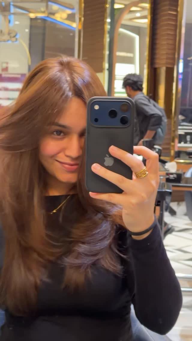 Woman displaying long, layered light honey-brown hair in a salon mirror selfie