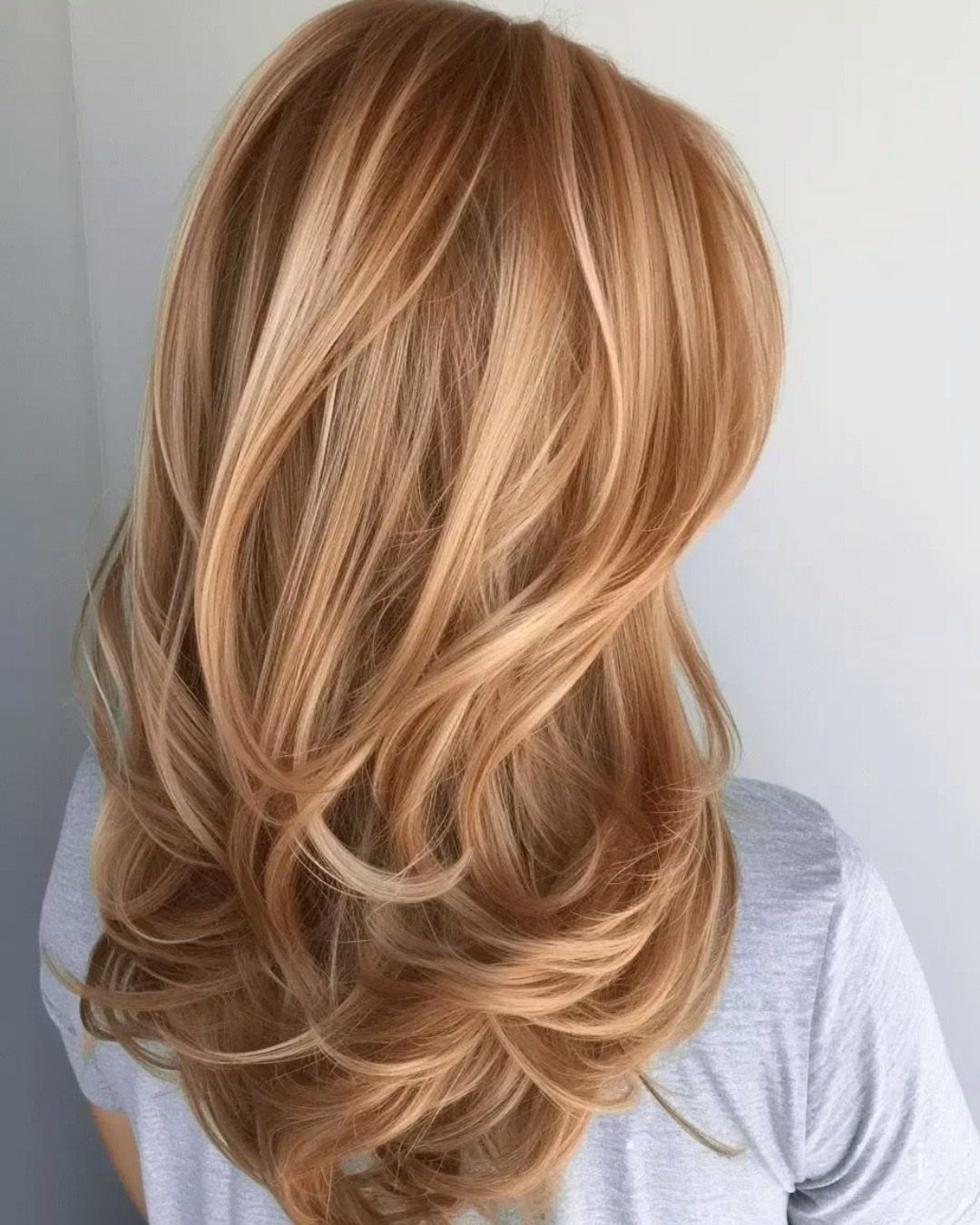 Layered honey brown hair with soft strawberry-gold highlights and curled ends