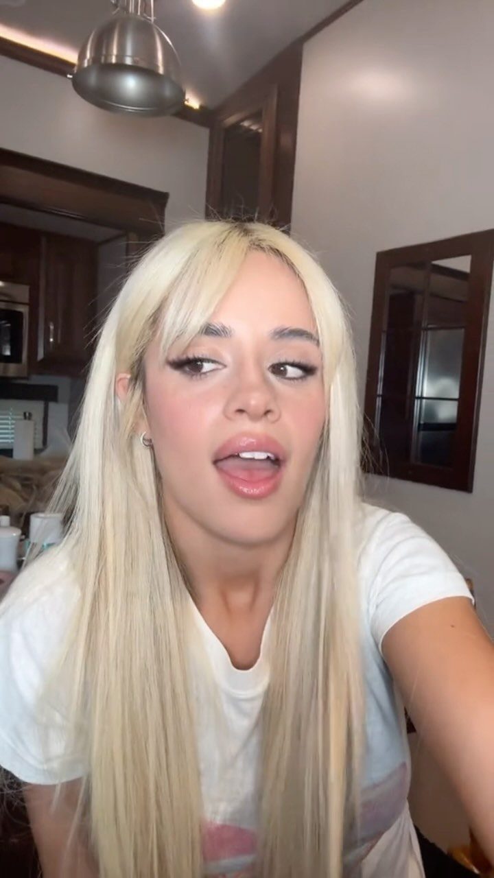 Long, straight pale blonde hair with bangs worn loose over a white T-shirt
