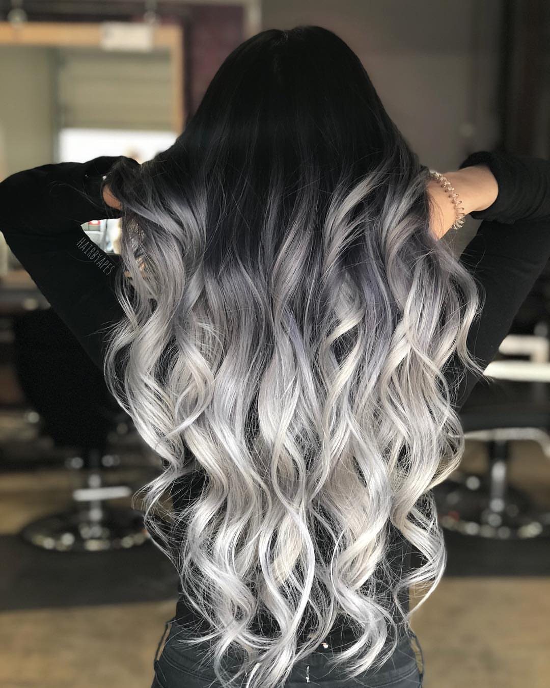 Long wavy ash icy blonde hair with dark roots displayed in a salon