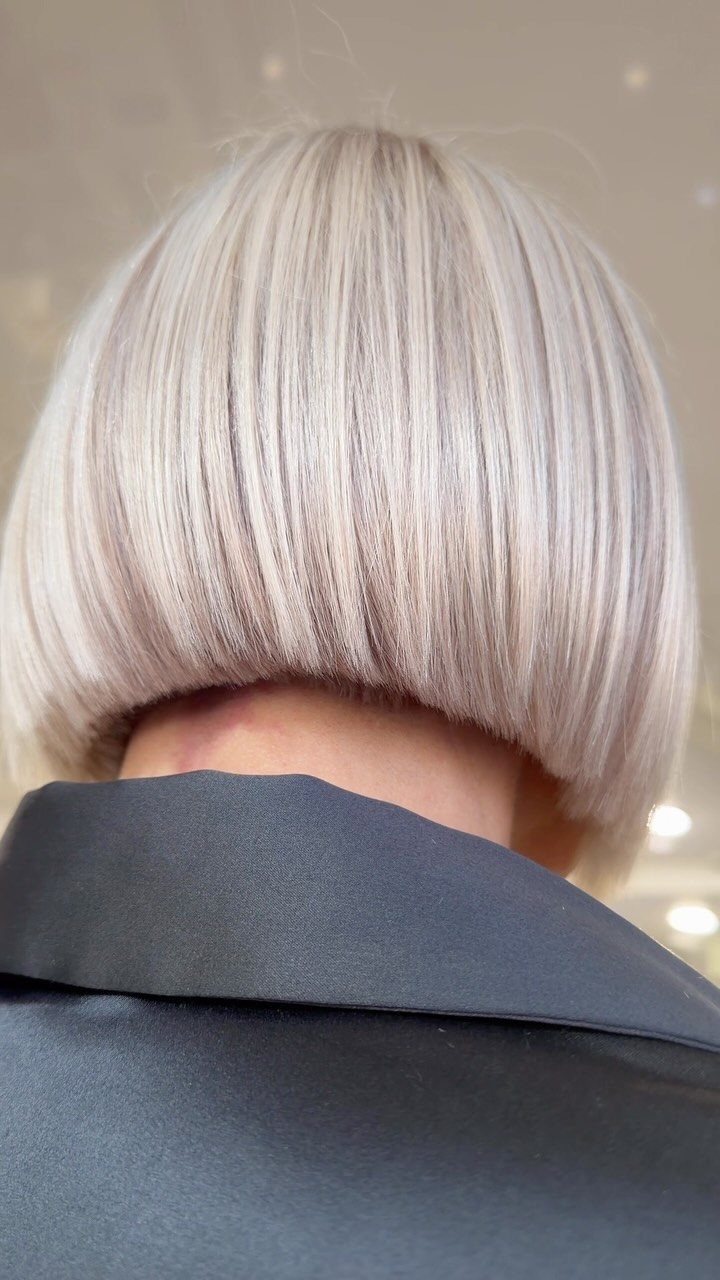 Blunt ice-blonde bob with straight fringe above a dark salon cape