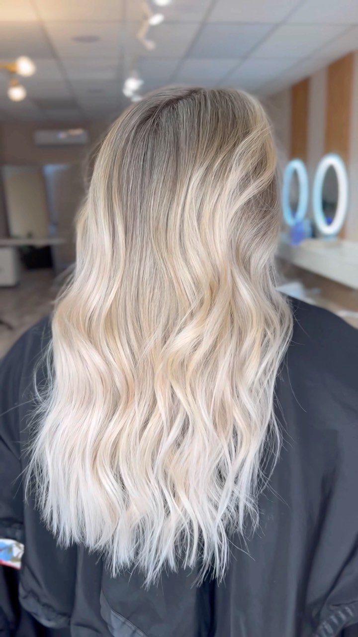 Long wavy blonde hair shows icy highlights blended through darker roots in a salon