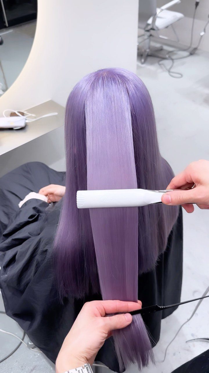 Long lavender-silver hair being straightened with a white flat iron in a salon.