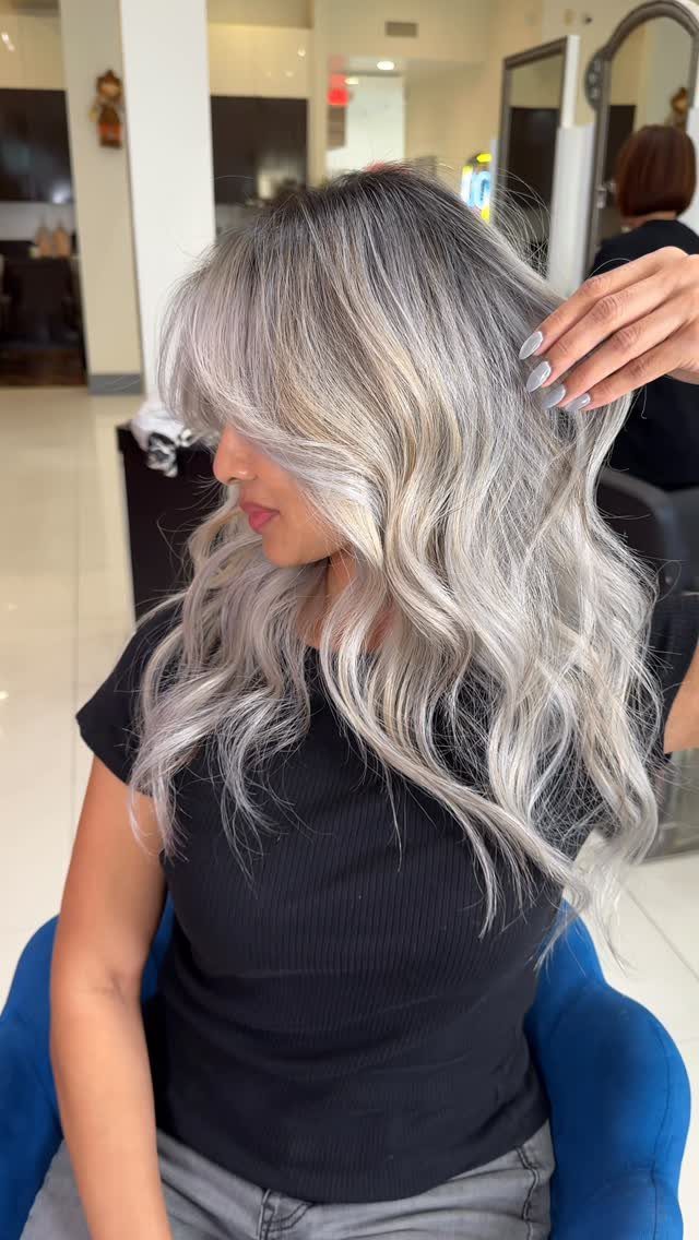 Woman showing long platinum waves with soft gray shadow roots in a salon