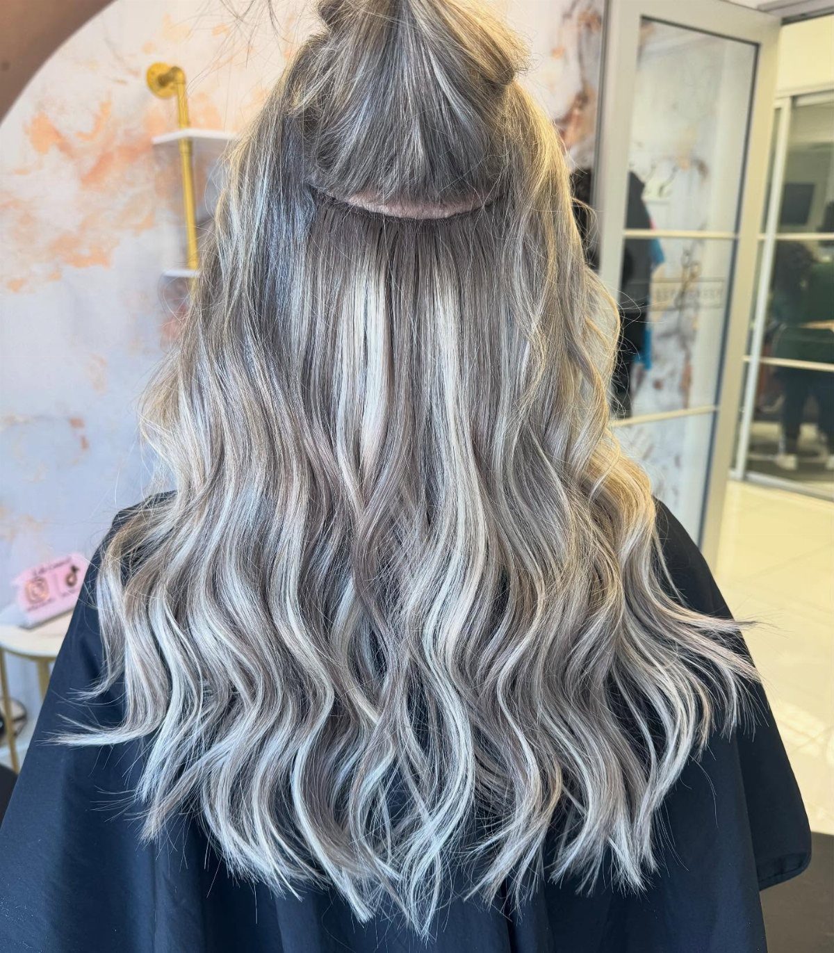 Long wavy platinum hair with smoky dark roots displayed from behind in a salon
