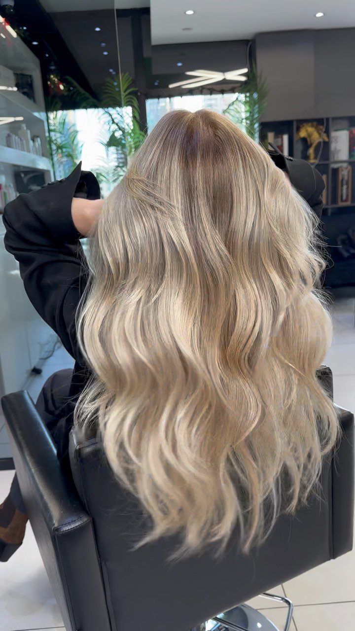 Long wavy blonde hair with beige roots and pale icy lengths in a salon chair