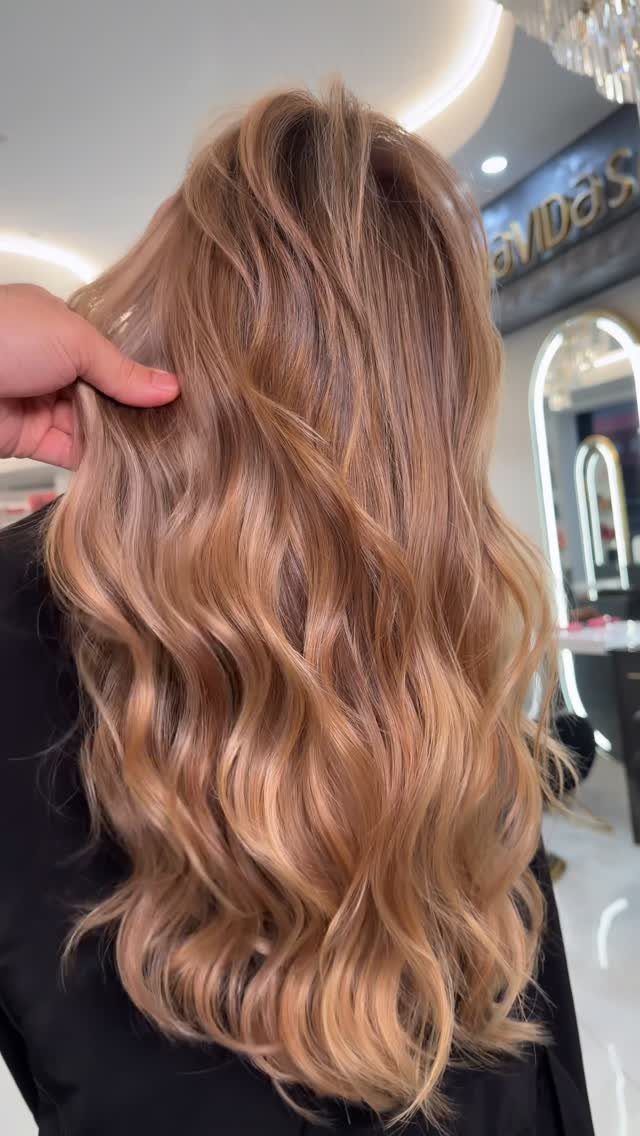 Long rose-gold blonde waves cascade down a salon client’s back