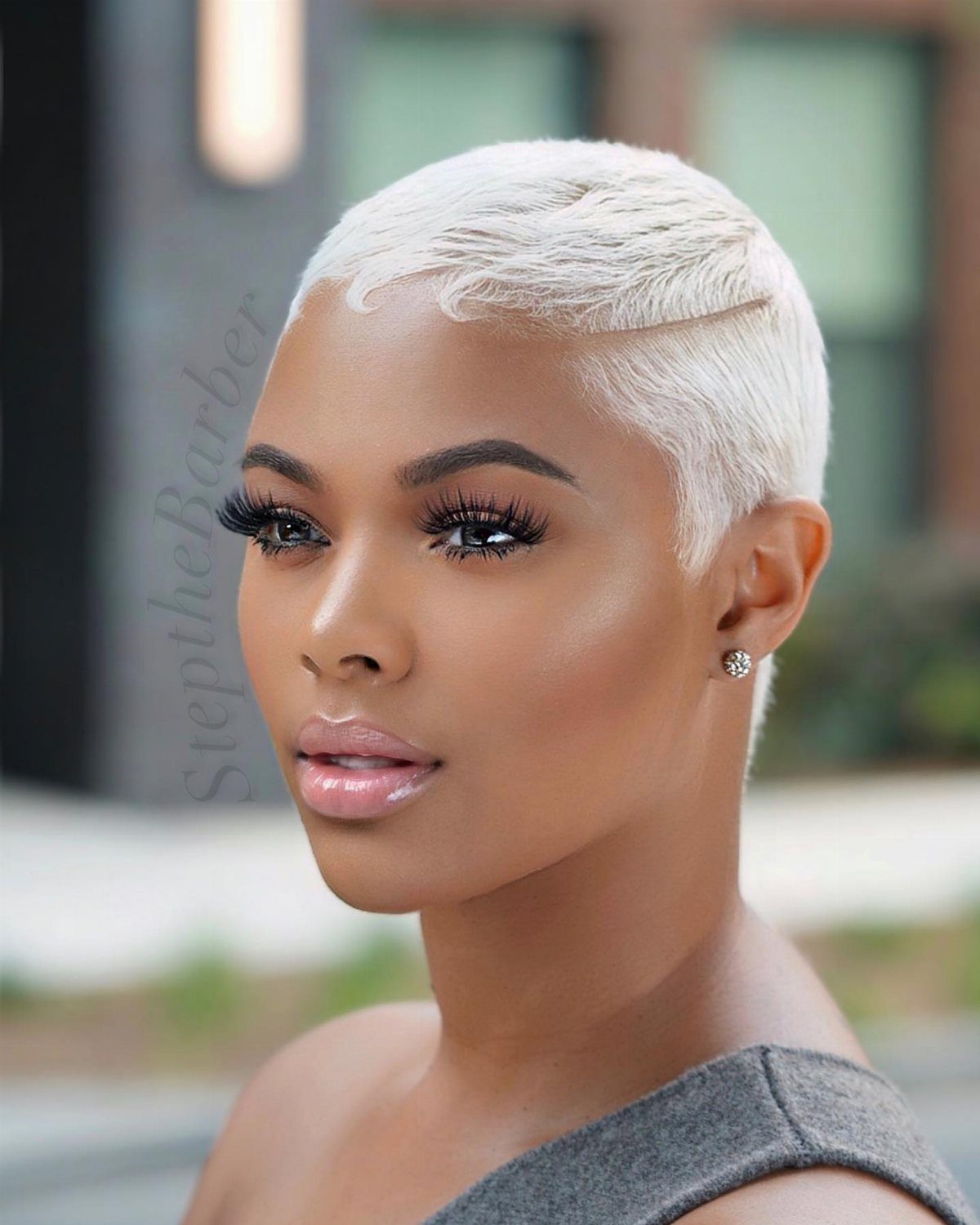 Person with an extra-short icy white-blonde pixie cut and gray top