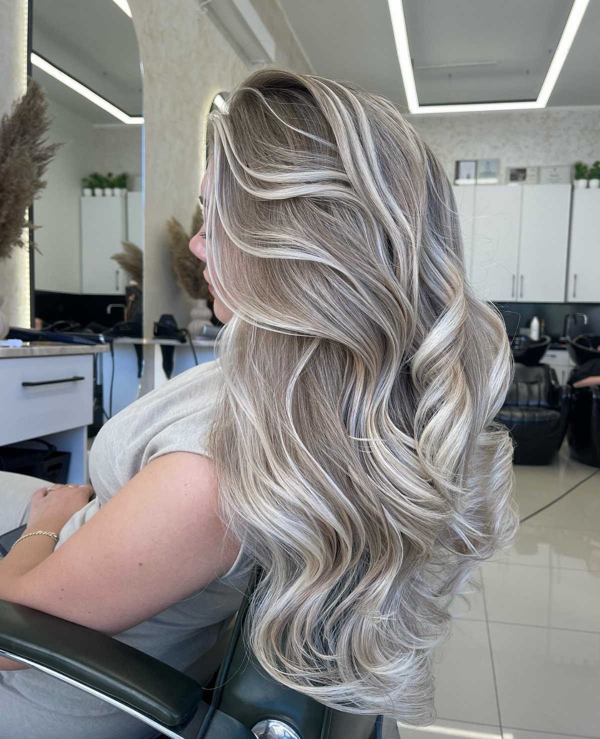 Long wavy hair showing icy ash-blonde balayage with darker roots in a salon