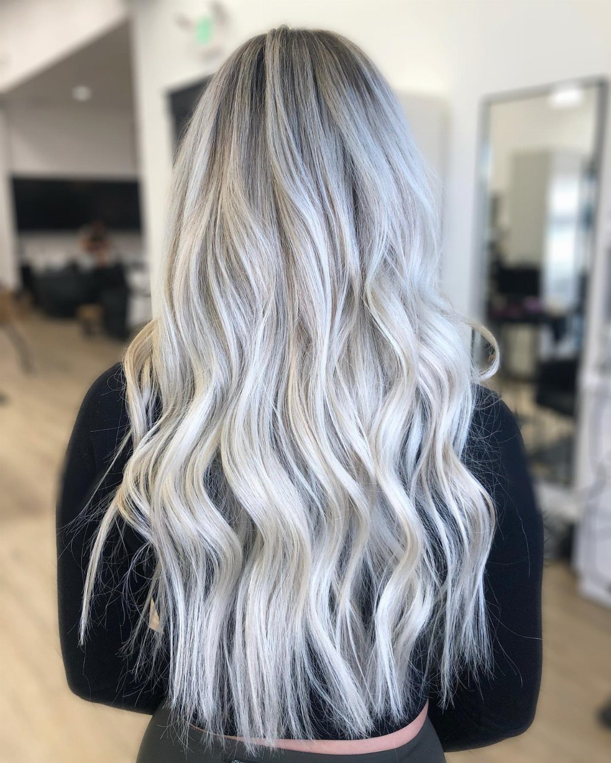 Long wavy icy blonde balayage hair with dark roots in a salon